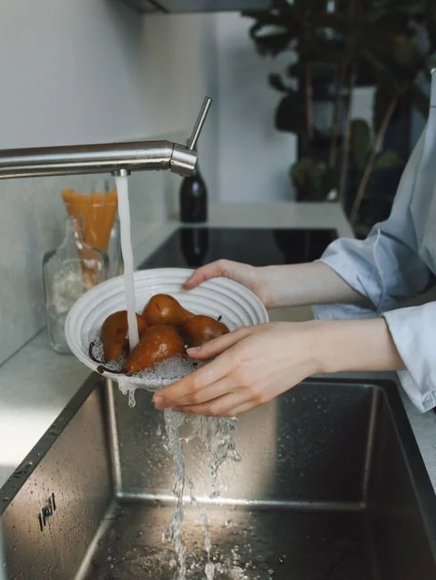 Close-up of gloved hands disinfecting a remote control with a cloth and spray bottle.